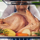 Turkey on a pan of vegetables being placed in the oven